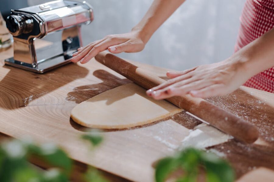 Hands rolling fresh pasta dough on a wooden board