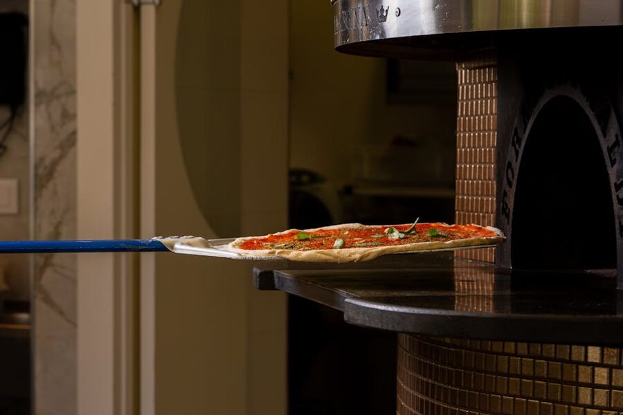 Pizza with fresh ingredients entering a wood-fired oven
