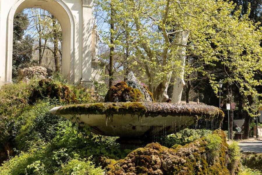 Sunlit historic fountain surrounded by greenery in a Rome villa garden