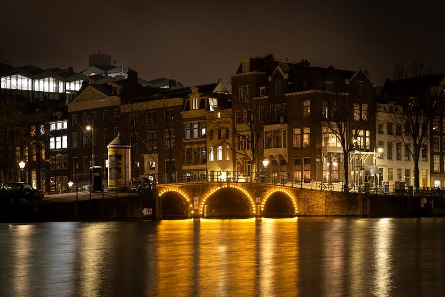 Amsterdam canal bridge at night with warm string lights reflecting on the water