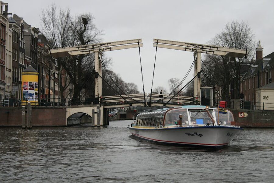Glass-roofed canal cruise boat passing under an arched stone bridge in Amsterdam