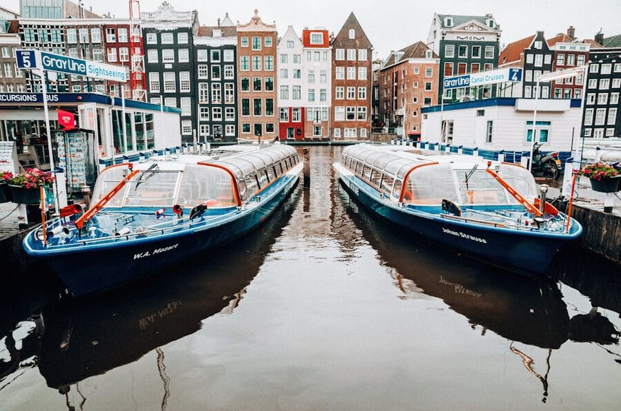 A row of glass-roofed Amsterdam canal tour boats moored at a pier waiting for passengers