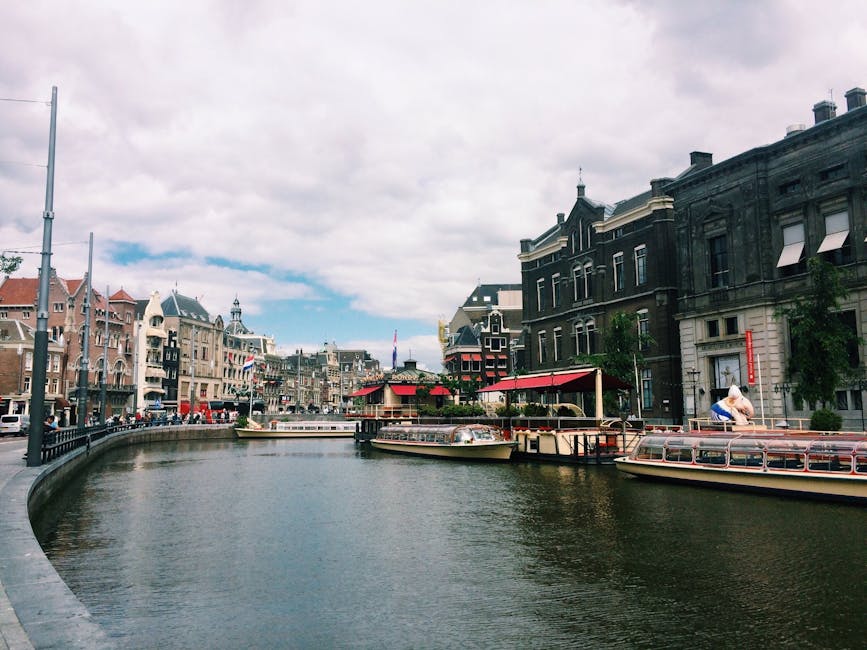 Multiple tour boats on a wide section of an Amsterdam canal showing the city architecture