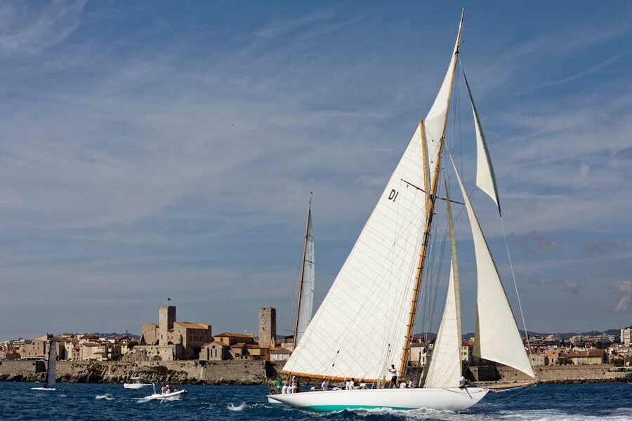 Sailboat passing Antibes old town with stone ramparts