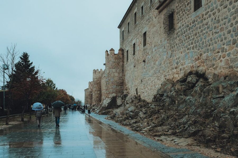 People walking by ancient Avila walls on a wet day