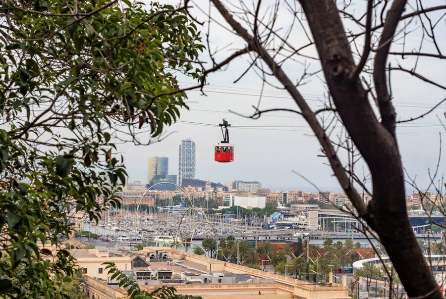 Red and white Port Cable Car of Barcelona seen through trees