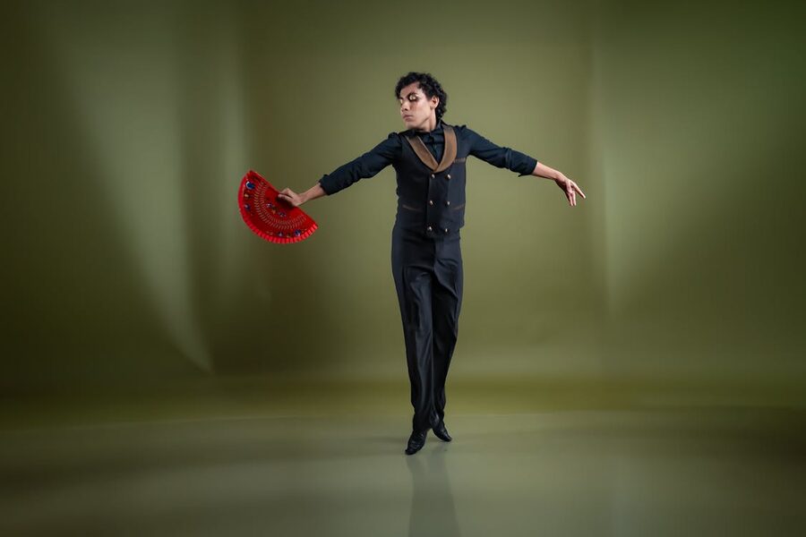 A flamenco dancer in a green-and-red costume with a hand fan