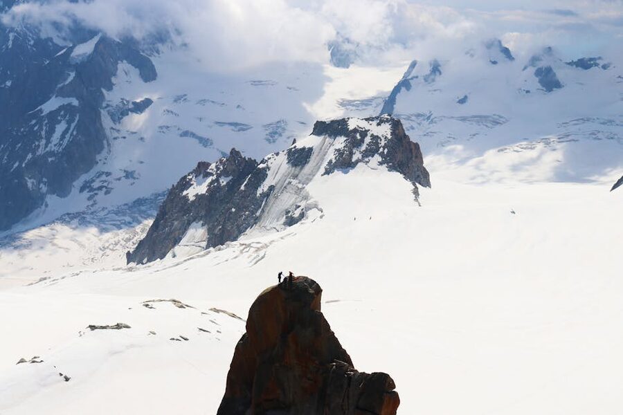 Two hikers atop a rock with Mont Blanc snowy expanse behind