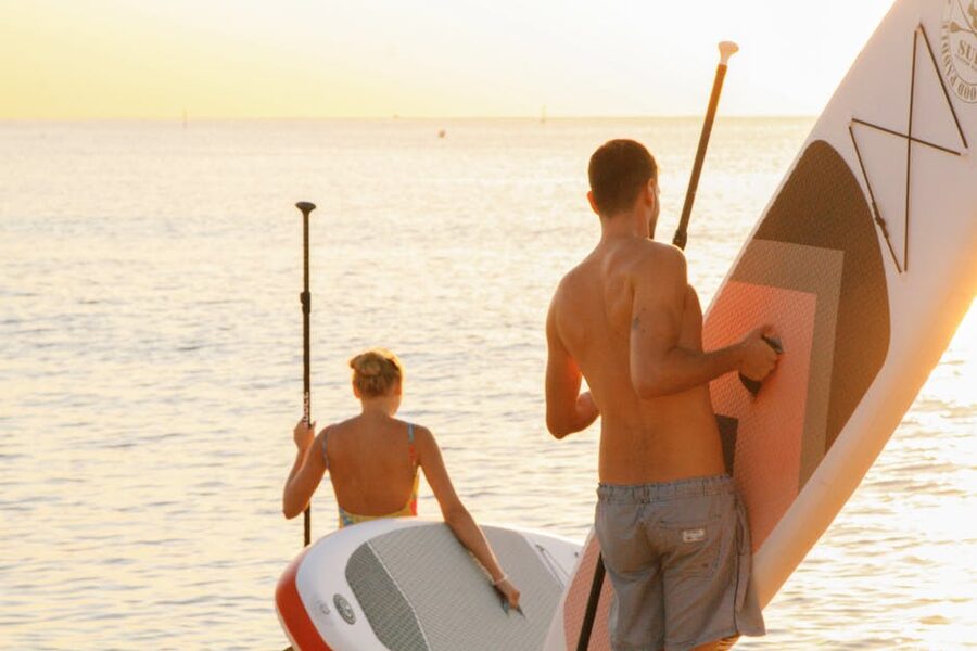 A couple paddleboarding at sunset on a serene beach