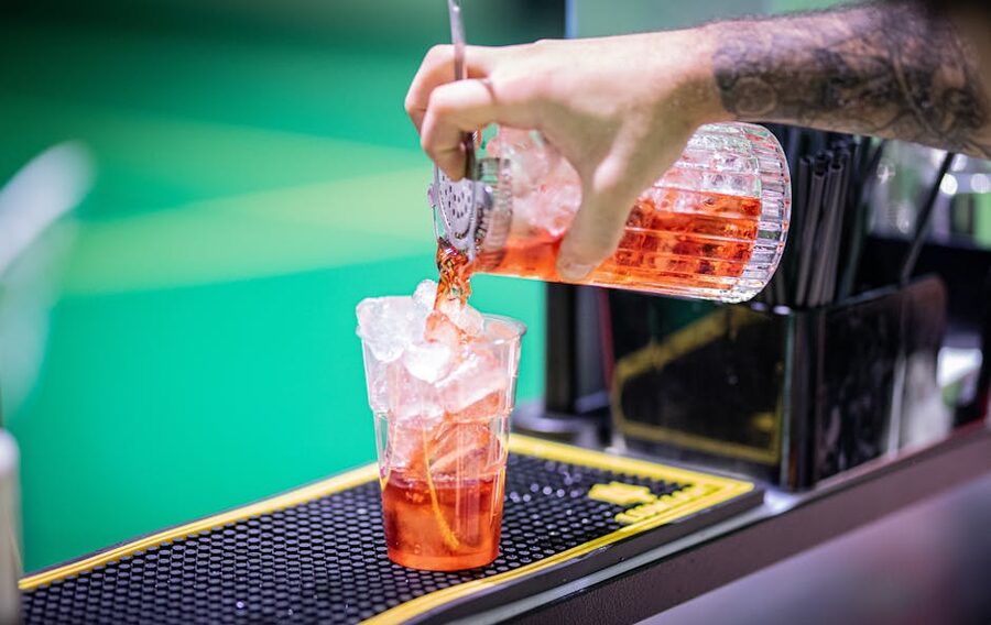 Bartender pouring red cocktail into a glass with ice