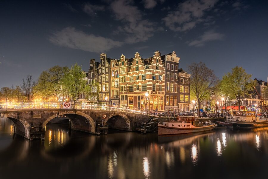 Amsterdam canal bridge lit at night with reflections in the water