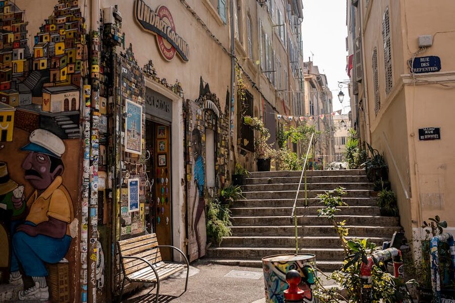Sunlit stairs in a Marseille alley with murals and lush plants