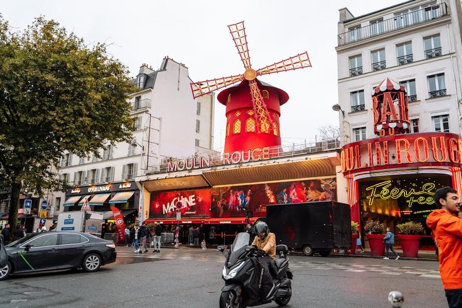 The Moulin Rouge surrounded by city traffic and historic Paris architecture