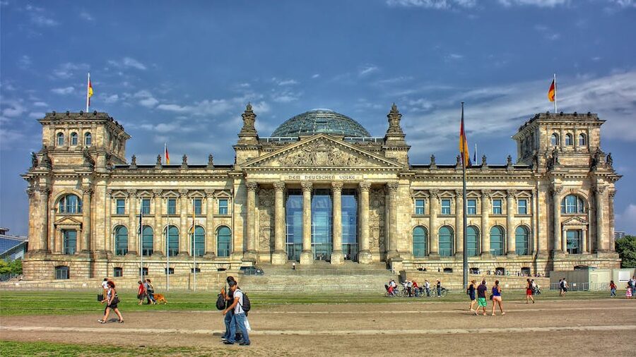 Front facade of the Reichstag with German flags and visitors on the lawn