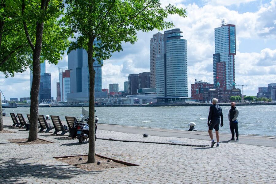 People walking the riverside promenade with the Rotterdam city skyline behind them