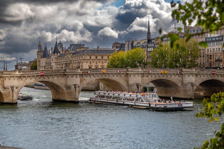 A glass-canopied Seine cruise boat passing under the historic Pont Neuf in Paris