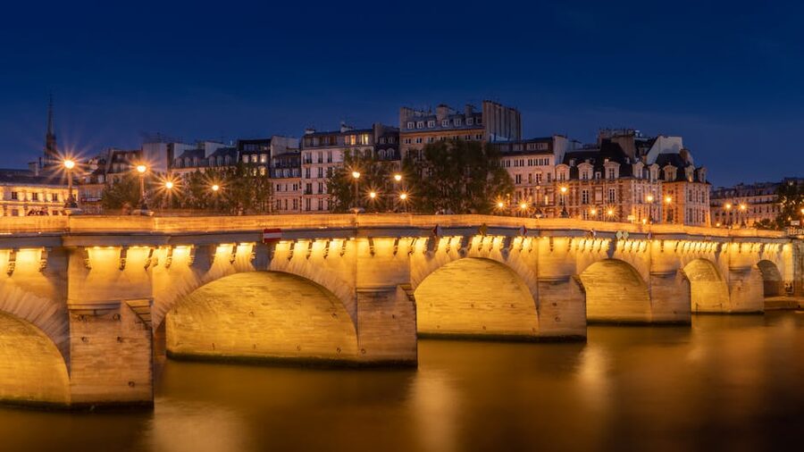Pont Neuf bridge illuminated at night reflecting on the Seine River in Paris