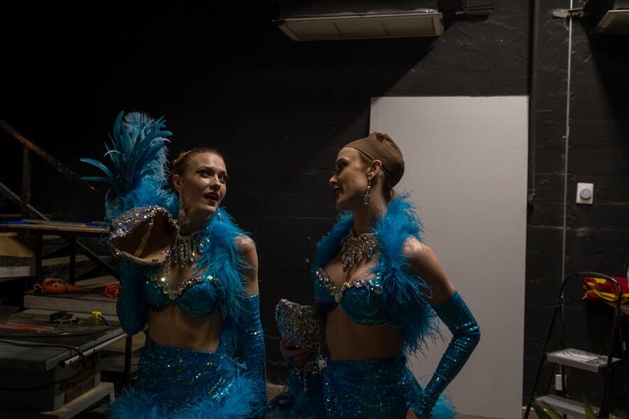 Two showgirls in blue sequin costumes preparing backstage at a cabaret