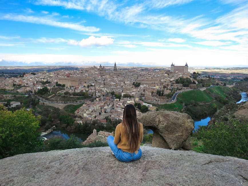 A traveller sits on a cliff at the Mirador del Valle looking across at the Toledo cityscape