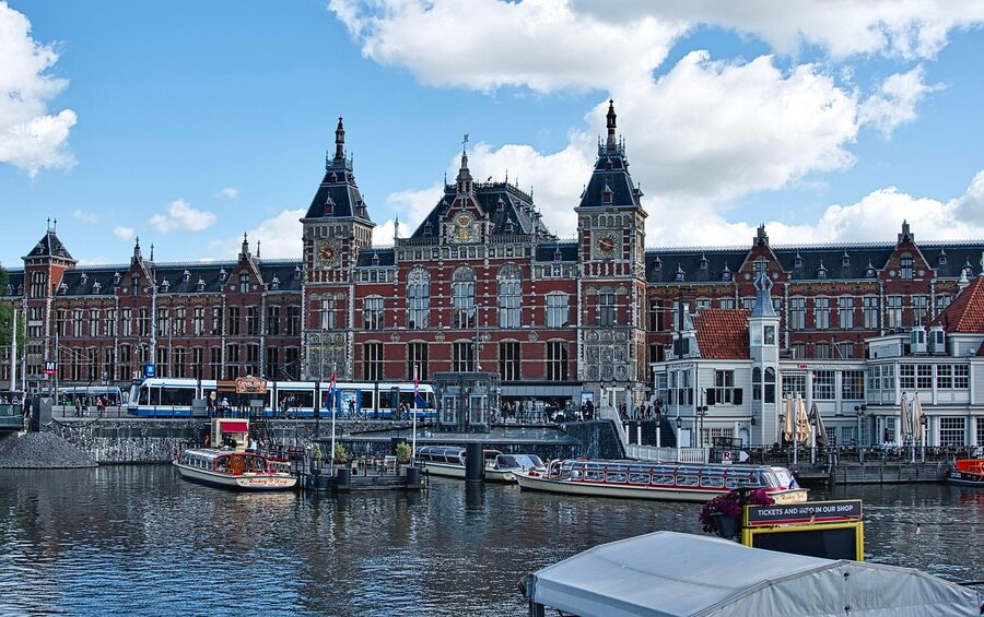 Amsterdam Centraal Station with cyclists and travellers in front, near the Upside Down Museum on Damrak