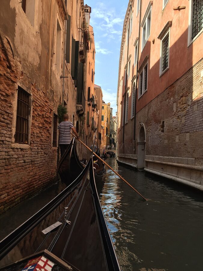 Black gondola squeezing through a very narrow Venetian side canal between tall buildings