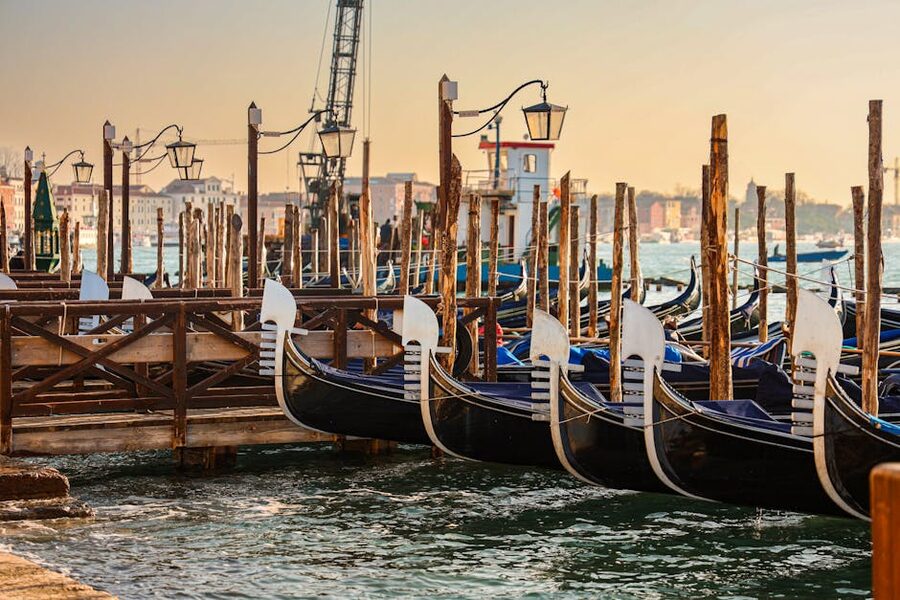 Row of gondolas moored at a Venice quay at dawn with golden light on the water