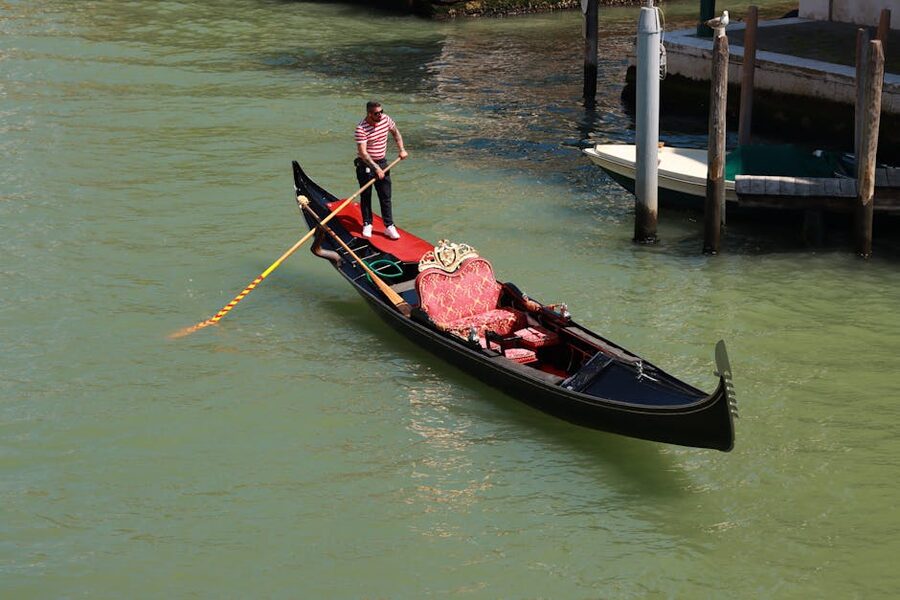 Venetian gondolier in striped shirt standing at the stern of his black gondola