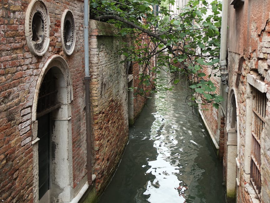 Quiet Venetian side canal with ancient brick walls and traditional moored boats